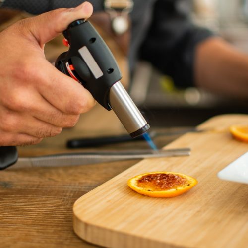 Barman burns orange with gas torch in bar for preparing cocktail. Profession concept.